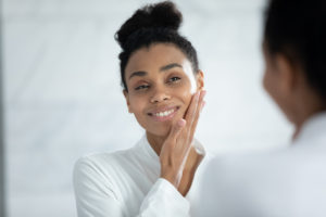 The image shows a beautiful woman standing in front of a mirror to show how to prepare for a brow lift.